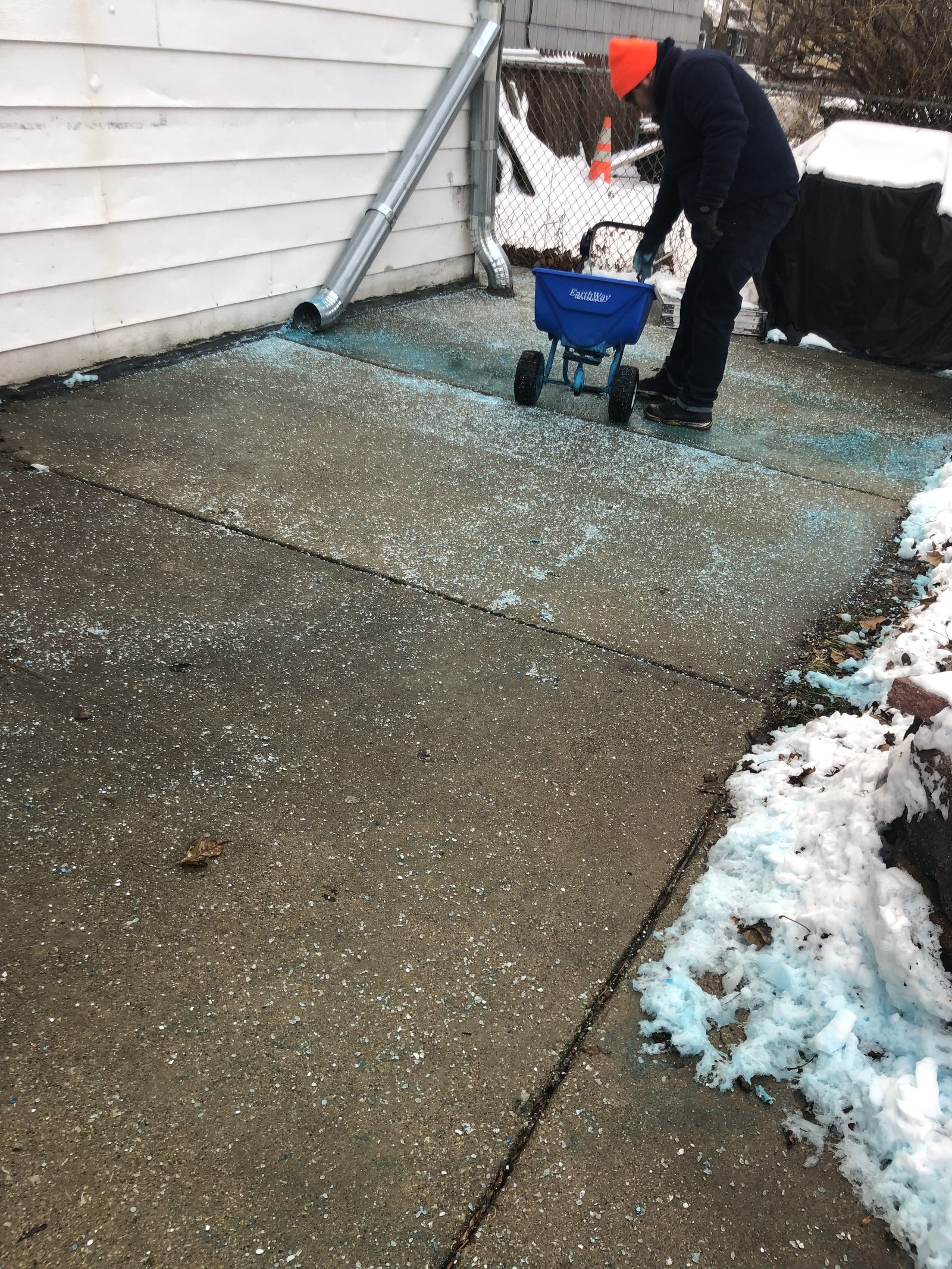 Snow Pushers crew member spreading ice melt on a Chicago concrete walkway using an EarthWay broadcast spreader